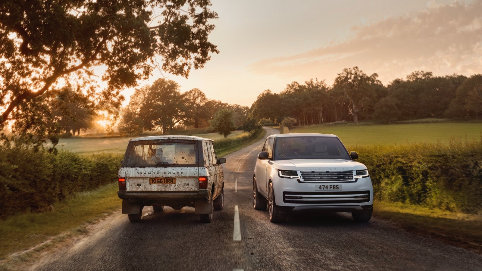 A mud-covered Range Rover Classic and the new electric Range Rover passing each other on an English country lane at sunrise.